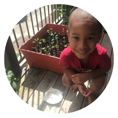 Young blind boy smiles and kneels down next to his NFB BELL seeds that are sitting in the sun