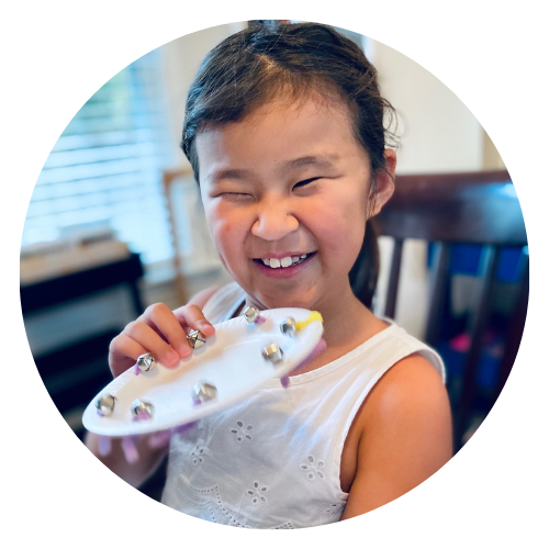 Young blind girl smiles and shakes homemade musical instrument.