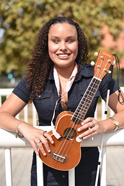 Picture of Precious Perez smiling leaning on a white rail holding a guitar