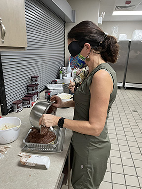 A student wearing sleepshades pours brownie mix into a baking pan.