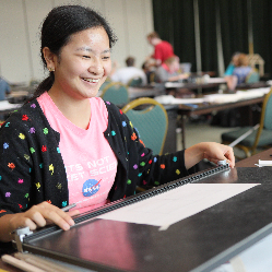 A student in NFB EQ working on a drawing design on a drafting table.