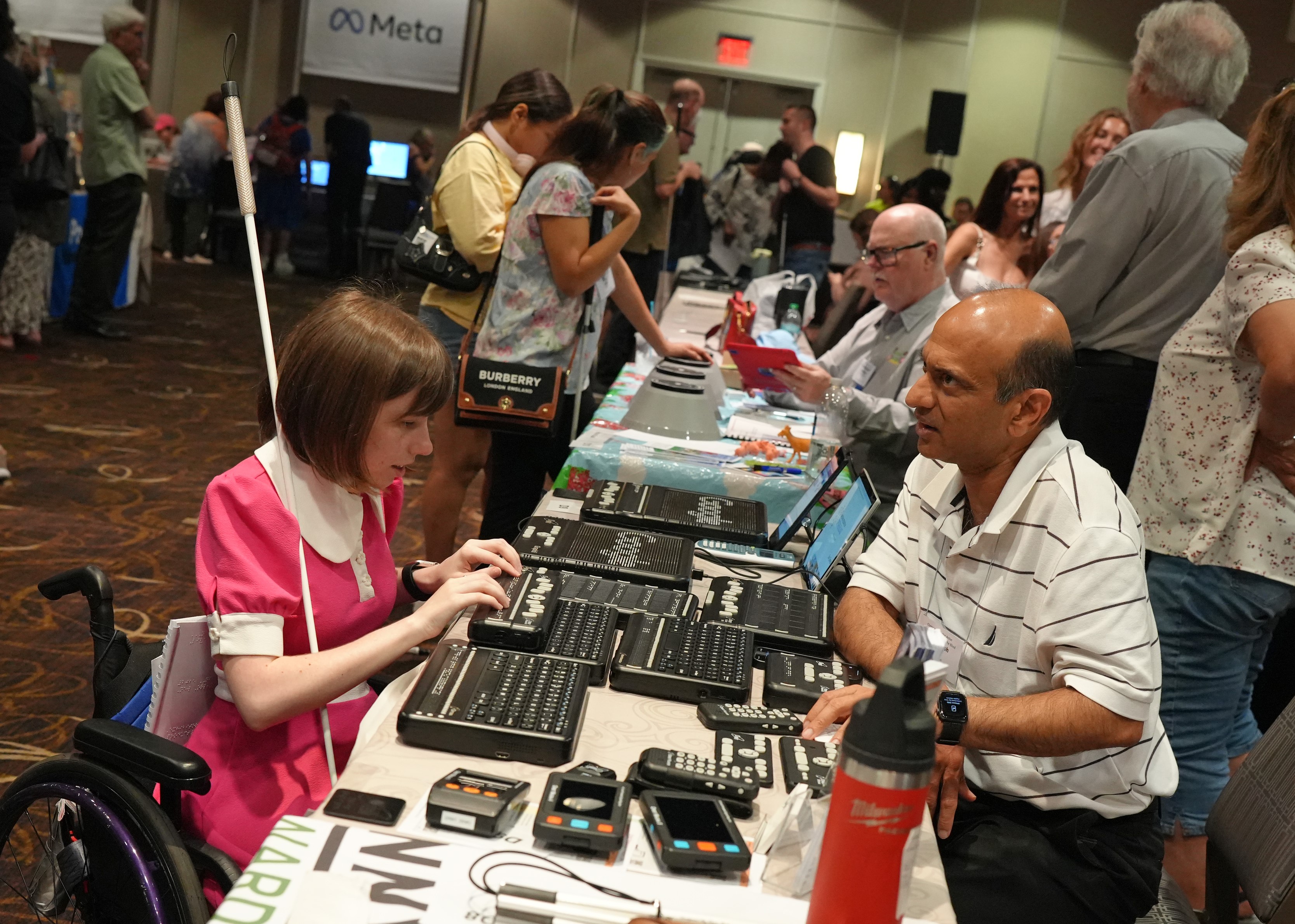 A woman in a wheelchair tests and discusses a product with an exhibitor.