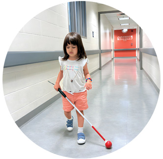 A toddler walks down the hall with her long white cane.