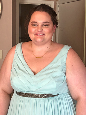 A portrait of Brittany with her hair in an updo and her makeup flawlessly done. She wears a formal light green v-neck dress.