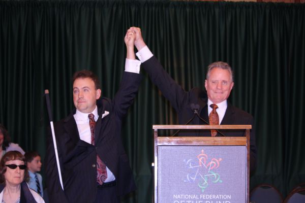 NFB President Mark A. Riccobono raises hands with Immediate Past President Marc Maurer at the 2014 National Convention.