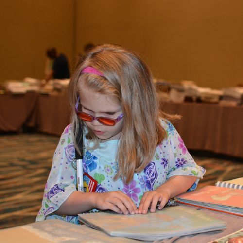 A young girl reads a Braille book at the 2018 National Convention. 