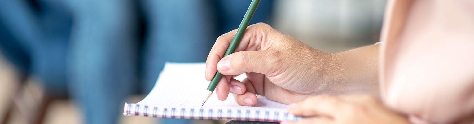 Close up of psychologist holding pen while making notes during a therapy session.