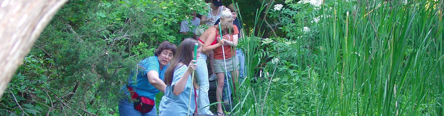 A group of blind teens and adult mentors hike through the woods.