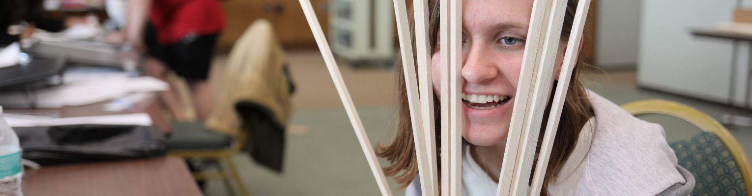 An NFB EQ student smiling behind several pieces of balsa wood.