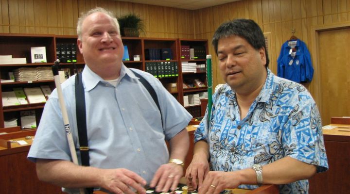 Two men stand in the Independence Market and play a game of Brailled checkers.
